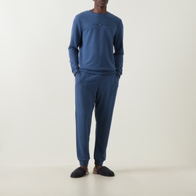 Model wearing blue long-sleeve top and matching tapered joggers, styled with dark slippers