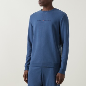 Model wearing blue Tommy Hilfiger crew neck sweatshirt with embroidered chest logo, styled with matching blue joggers