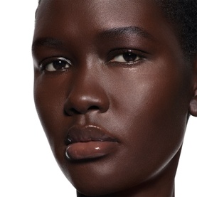 Model wearing Victoria Beckham Posh Gloss in Bikini, a sheer nude-pink lip gloss finish on deep skin tone