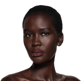 Model wearing Victoria Beckham Posh Gloss in Bikini, a sheer glossy lip shade, with bare shoulders against white background.