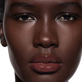 Model wearing Victoria Beckham Posh Gloss in Bikini, a sheer nude-brown lip gloss, with subtle glittery eye liner detail