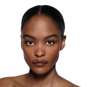 Model wearing Victoria Beckham Posh Gloss in Bikini, a sheer nude-pink lip gloss, with a sleek updo and bare shoulders.
