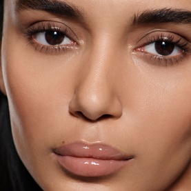 Model wearing Victoria Beckham Posh Gloss in Bikini, a sheer nude-pink lip gloss with a glossy finish, paired with natural glowy makeup.