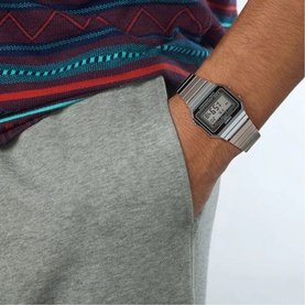 Model with Casio silver-tone digital watch with square face and metal bracelet strap, styled with grey joggers and striped top
