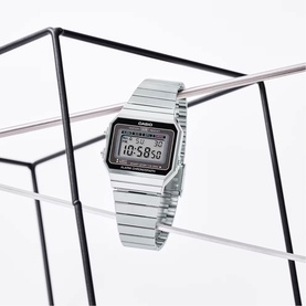Casio silver-tone digital watch with rectangular LCD display and stainless steel bracelet, displayed on a geometric glass frame