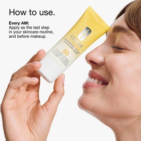 Model with Clinique UV Solutions Brightening + Tinted Sunscreen SPF 50 in Light, held close to face, tube format