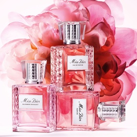 Dior Miss Dior Eau de Parfum Roller-Pearl shown with Miss Dior Blooming Bouquet bottles, styled with pink roses in background.