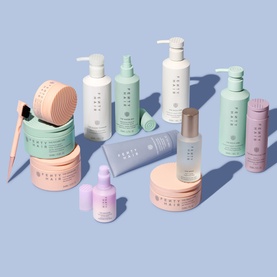 Fenty Hair full collection displayed together, featuring pumps, jars, tubes and serums in pastel mint, peach and lilac packaging on a blue background.