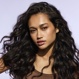 Model with voluminous, wavy dark hair styled after using Fenty Hair Dry Shampoo, wearing a brown top