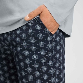 Hanro Celestial Night pyjama bottoms in navy geometric print, worn with light grey top, hand resting in pocket.