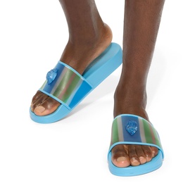 Model wearing Kurt Geiger London blue iridescent slide sandals with chunky flatform sole and embossed eagle logo on strap.