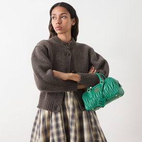 Model carrying Miu Miu Arcadie Matelass&eacute; Top Handle Bag in Mango with gold-tone hardware, styled with brown knit cardigan and plaid skirt