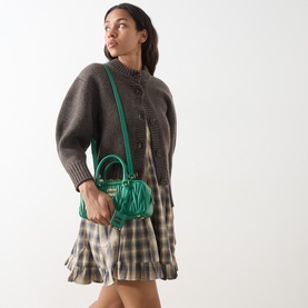 Model carrying Miu Miu Arcadie Matelass&eacute; Top Handle Bag in Mango green, gold-tone hardware, worn crossbody over grey knit and plaid mini dress.