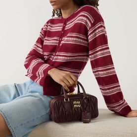 Model carrying Miu Miu Arcadie Matelass&eacute; Small Top Handle Bag in bordeaux with gold-tone hardware, styled with a red striped cardigan and blue jeans.