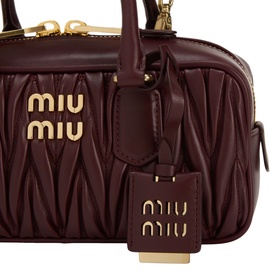 Miu Miu bordeaux matelass&eacute; leather crossbody bag with gold-tone hardware, logo lettering, and branded luggage tag charm.