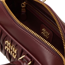 Miu Miu bordeaux leather crossbody bag, open view showing gold zip, quilted interior lining and embossed logo charm
