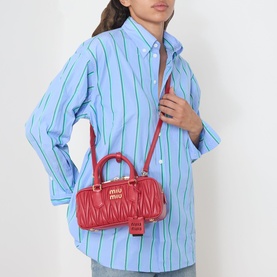 Model carrying Miu Miu Arcadie Matelass&eacute; Top Handle Bag in Rosso red leather, gold-tone hardware, worn crossbody over blue striped shirt.