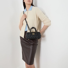 Model carrying Miu Miu Arcadie Matelass&eacute; Small Top Handle Bag in Nero, gold-tone hardware, worn crossbody with cream knit cardigan and brown leather