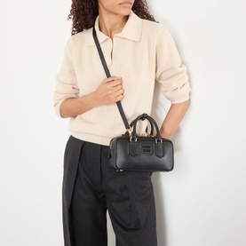 Model carrying Miu Miu Arcadie Small Top Handle Bag in Nero black leather with gold-tone hardware and detachable crossbody strap, styled with cream