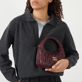 Model carrying Miu Miu Arcadie Matelass&eacute; Crossbody Bag in bordeaux with gold-tone hardware and matelass&eacute; finish, styled with grey coat.