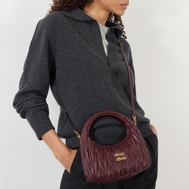 Model carrying Miu Miu Arcadie Matelass&eacute; Crossbody Bag in bordeaux with gold-tone hardware, worn as crossbody over grey knit sweater.