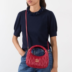 Model carrying Miu Miu Wander Matelass&eacute; Crossbody Bag in Rosso with gold-tone hardware and adjustable strap, styled with navy top and jeans.