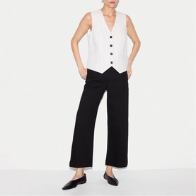 Model wearing Jigsaw black wide-leg cropped trousers with white button-front waistcoat and black flat loafers.