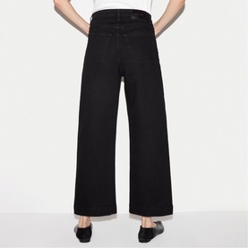 Model wearing Jigsaw black wide-leg jeans, rear view, with black flat shoes.