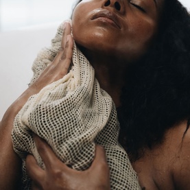 Model with Voya mesh exfoliating body bag held against neck and chest, shown in use against bare skin