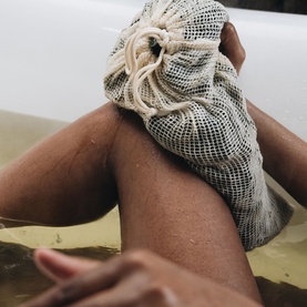 Voya mesh drawstring bath bag held against wet legs in a bath, shown in a lifestyle setting