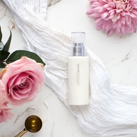 Voya Cleanser white pump bottle on marble surface, styled with pink roses, dried flower and gold spoon