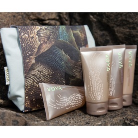 Voya bodycare gift set with three tubes and pale blue printed wash bag, displayed on natural stone surface