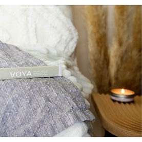 Voya Pillow Heaven Relaxing Sleep Spray 10ml resting on grey textured cushions beside a lit candle, cosy lifestyle setting