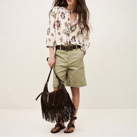 Model wearing Bash cream floral print blouse with khaki shorts and brown belt, carrying fringed suede shoulder bag with flat sandals