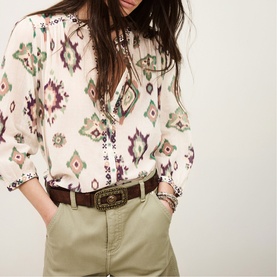 Model wearing Bash cream ikat-print blouse with V-neckline, styled with sage green trousers and brown leather belt.