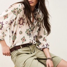 Model wearing Bash cream ikat-print blouse with khaki shorts, brown belt, and layered bracelets