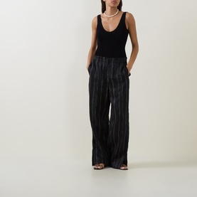 Model wearing Bond Eye black recycled swimsuit styled with wide-leg striped trousers, pearl necklace and strappy sandals.