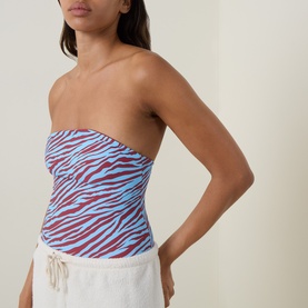 Model wearing Bond Eye swimsuit in blue zebra and ruby print, strapless bandeau style, styled with white drawstring shorts
