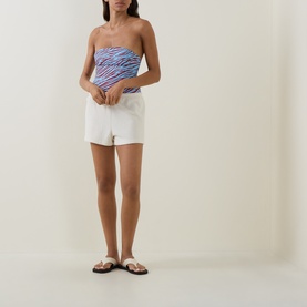 Model wearing Bond Eye swimsuit in blue zebra print bandeau style, styled with white shorts and tan flat sandals