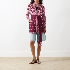 Model wearing burgundy and pink heart-pattern knit longline cardigan with tie belt, styled with light blue shorts and tan sandals