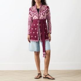 Model wearing burgundy and pink patterned knit belted cardigan coat, styled with light blue denim shorts and brown flat sandals