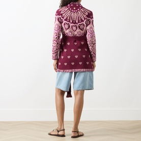 Model wearing burgundy and pink heart and floral jacquard knit cardigan, styled with light blue denim shorts and tan sandals, back view.