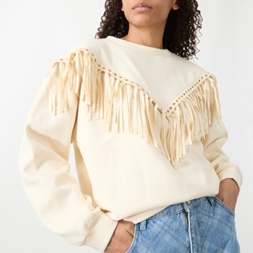 Model wearing Hayley Menzies Sabina Fringe Sweatshirt in ecru with chevron faux-suede fringing and gold eyelets, styled with blue jeans