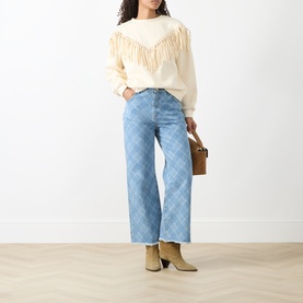 Model wearing Hayley Menzies Sabina Fringe Sweatshirt in Ecru with faux-suede fringing, styled with light blue check wide-leg jeans and tan boots.
