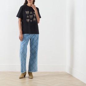 Model wearing Hayley Menzies black cotton T-shirt with leopard head graphic print, styled with light blue check trousers and tan ankle boots.