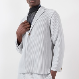 Model wearing Issey Miyake Pleated Single-Breasted Blazer in grey, notched collar, single-breasted, styled with dark ribbed turtleneck.
