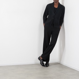 Model wearing Issey Miyake black polyester blazer with matching wide-leg trousers and black patent loafers.