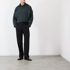 Model wearing Issey Miyake dark green pleated casual shirt with black tailored trousers and black loafers.