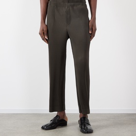 Model wearing Issey Miyake Pleated Wide Leg Trousers in brown with textured pleat detail, styled with black leather loafers.