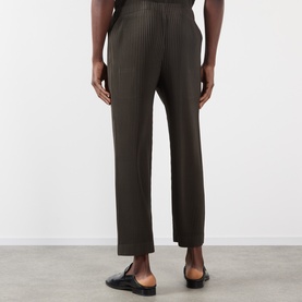 Model wearing Issey Miyake Pleated Wide Leg Trousers in brown, shown from behind, with black loafers visible at hem.